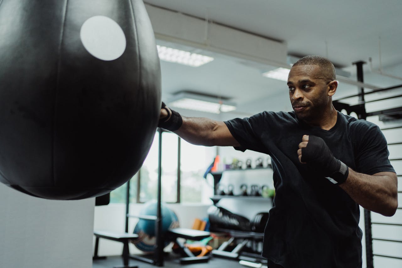 A Man in Black Shirt Working Out Using a Punching Bag